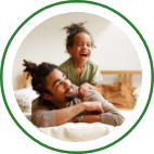 A young daughter lays on her dad’s back, laughing.  
